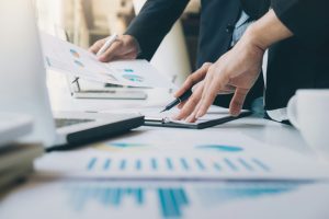 Työpöydällä on asiakirjoja ja kannettava tietokone, kun päätöksiä valmistellaan huolellisesti.