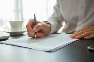 Henkilö istuu työpisteellä mietteliäänä ja arvioi työhön liittyvää päätöstä tai ongelmaa, ja kirjoittaa samalla.